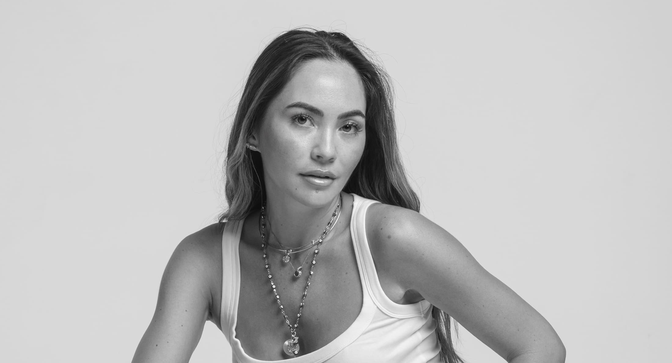 Linda Hausser crouching in a white tank and light denim, black and white studio portrait.